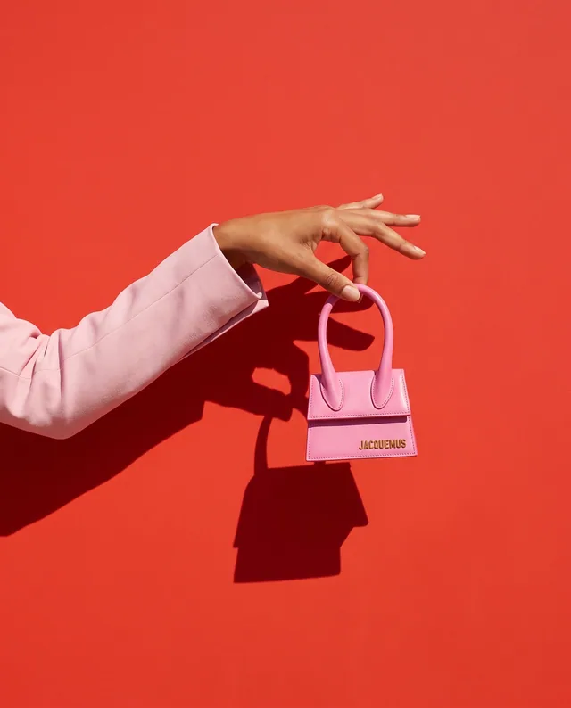 Un mini-sac rose porté à la main sur un fond rouge, dans une lumière franche.
