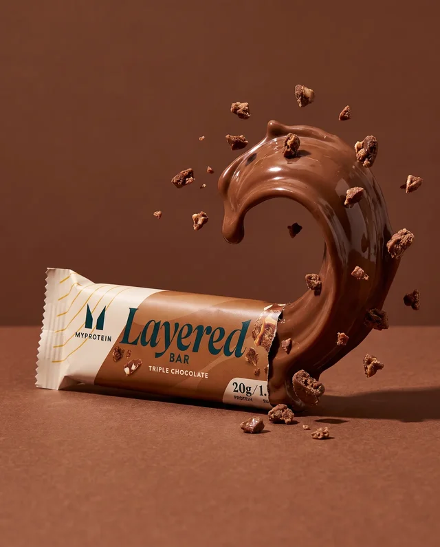 Une courbe de chocolat et des éclats croquants prolongent la barre dans un décor brun.