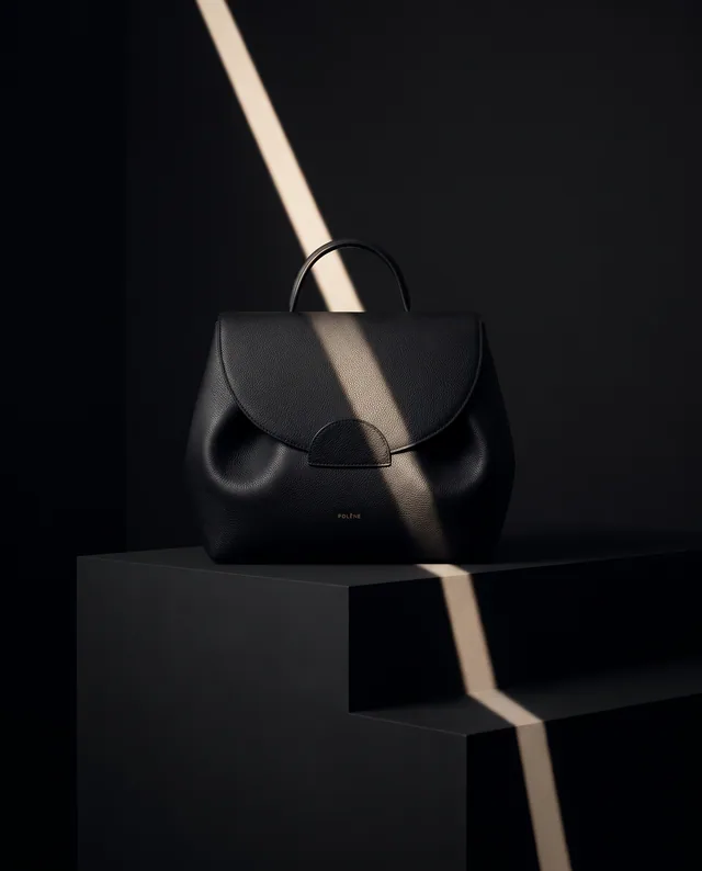 Un sac noir révélé par un faisceau de lumière, entre cuir grainé et lignes architecturales.
