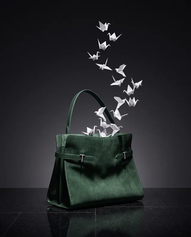 Un sac vert profond laisse s’envoler des oiseaux de papier dans un décor sombre.