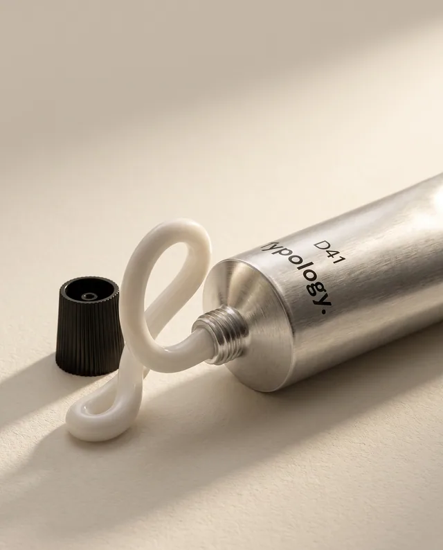 Une courbe de crème prolonge le tube métallique dans une lumière naturelle.